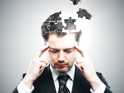 A business suit with his eyes closed, focusing intently. His head is visualized as an incomplete jigsaw puzzle, with several pieces floating above him, symbolizing the concept of putting thoughts or ideas together