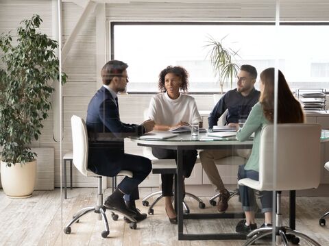 Four people in a cabin sitting on chairs near a round table are having a discussion