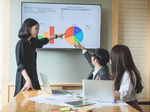 Three people were in the meeting room; one of them was presenting some data, and the other was writing points and asking something