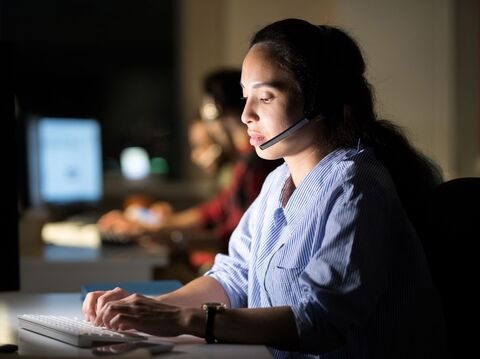 A girl sitting in a office working on a screen and wearing headphones