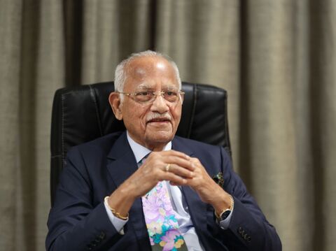 Portrait of an elderly businessman in a suit and tie, sitting in an office chair and smiling, likely during an interview or meeting