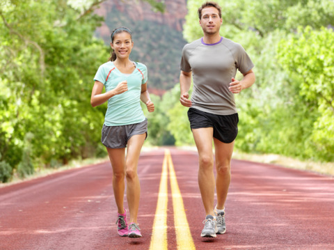 A woman and man jogging on a track both dressed in shorts