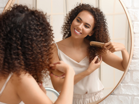 A woman with curly hair brushing her hair looking into the mirror