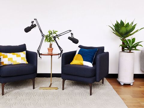 A cozy podcast studio setup with two chairs, microphones on adjustable arms, and decorative pillows