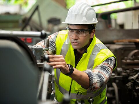 A construction worker in a hard hat and vest working on machinery