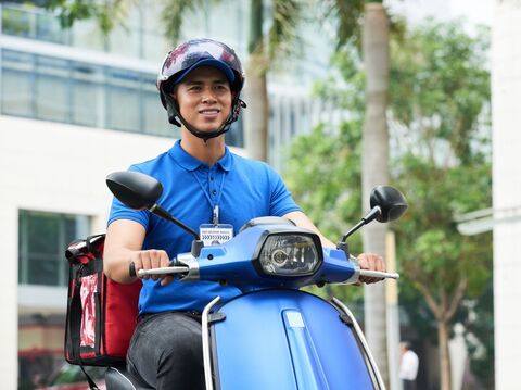 Delivery service worker on a blue scooter wearing a helmet and a company uniform, ready to dispatch parcels in an urban setting