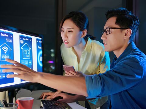 Two professionals, a woman and a man, discussing and interacting with a smart home control interface in a dark office