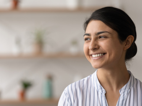 Smiling woman looking into the distance, set against a softly blurred background of a modern, minimalist room with subtle decor elements