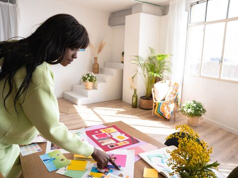Woman in a light green sweater working on a colorful design layout in a bright, plant-filled modern room