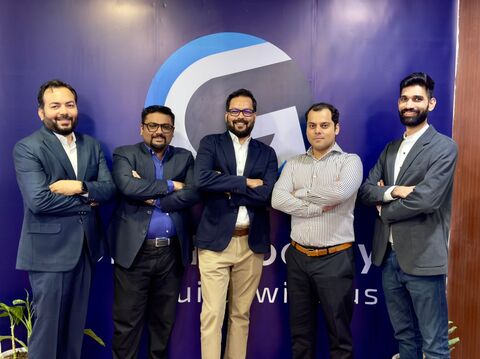 A group of five men in business attire standing together with their arms crossed, smiling at the camera, in front of a dark blue background with a large logo