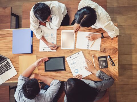 Top view of a team of professionals working together around a wooden table, discussing charts and reports, highlighting the role of digital marketing in brand perception