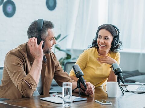 A man and woman, both wearing headphones, engaging in a lively conversation while recording a podcast in a modern studio environment