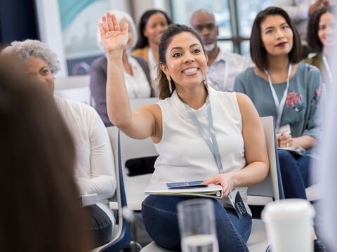 Enthusiastic woman raising her hand in a meeting, surrounded by attentive colleagues in a bright conference room