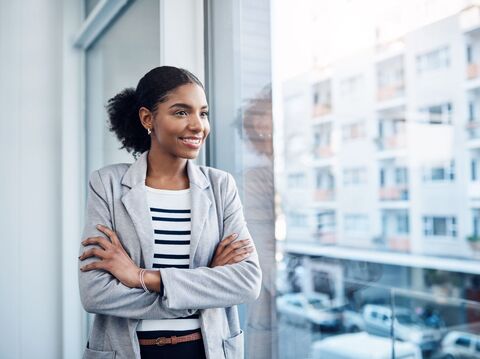 Confident businesswoman smiling while looking out the window of a modern office building