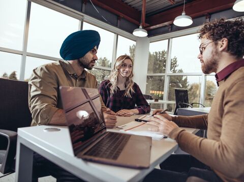 Three professionals engaged in a discussion in a bright, modern office, with a laptop open on the table