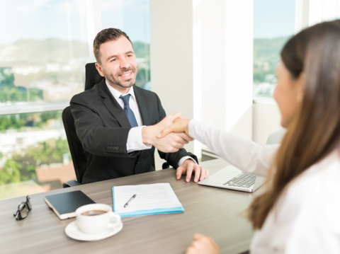 Business professional shaking hands with a client across a desk, symbolizing successful negotiation