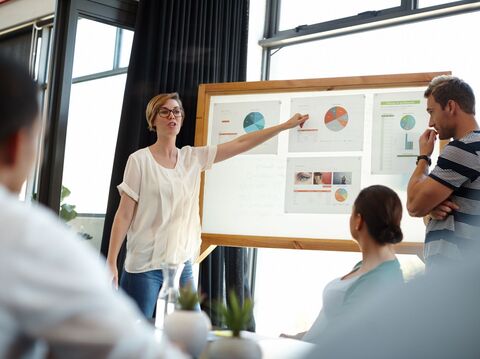 In a meeting room, a woman is explaining some graphs to other team members