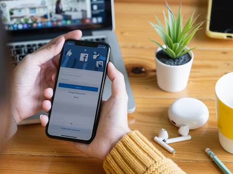 A person holding a smartphone with the Facebook login screen displayed