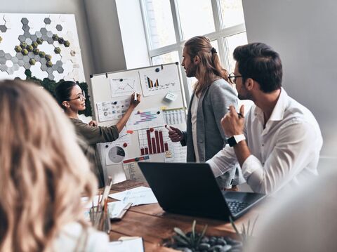 In a meeting room, a woman is explaining some graphs to people