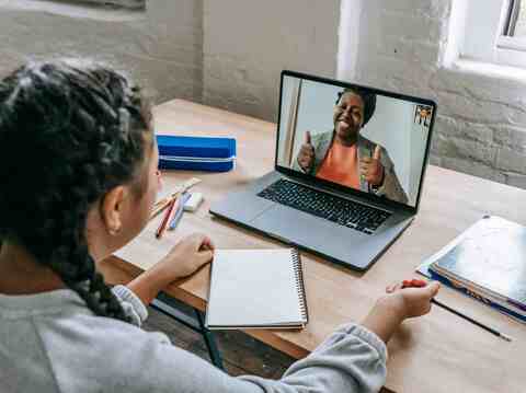 Student engaging in an online class with a smiling teacher on a laptop screen, demonstrating remote learning