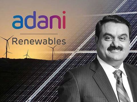 Portrait of Gautam Adani in front of the Adani Renewables logo, with a background of wind turbines and solar panels at sunset