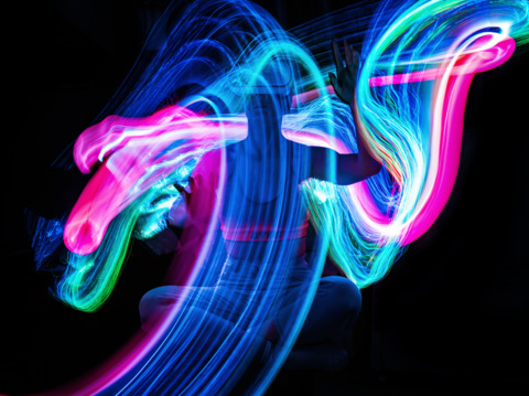 A long exposure photo of a woman wearing a virtual reality headset. She is surrounded by colorful neon signs and lights