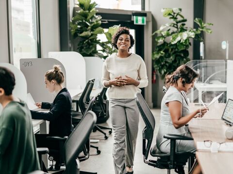 Woman with curly hair standing and smiling in office space with workstations