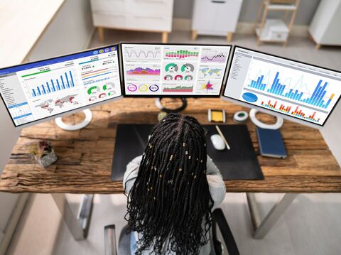 Woman analyzing complex data visualizations on multiple monitor screens