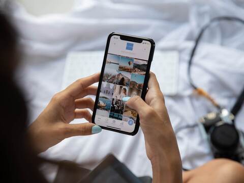 Person's hands holding smartphone displaying travel photos grid