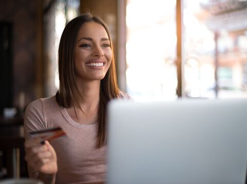 A woman is sitting in her room, watching her laptop, and holding a card