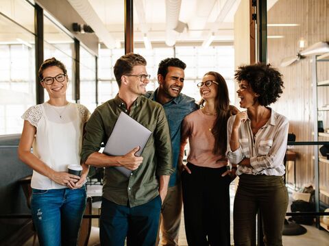 A group of people standing in an office area and smiling by looking at each other