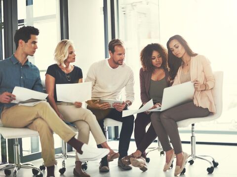 A diverse group of five young professionals, including three women and two men, engaged in a collaborative meeting in a modern office setting