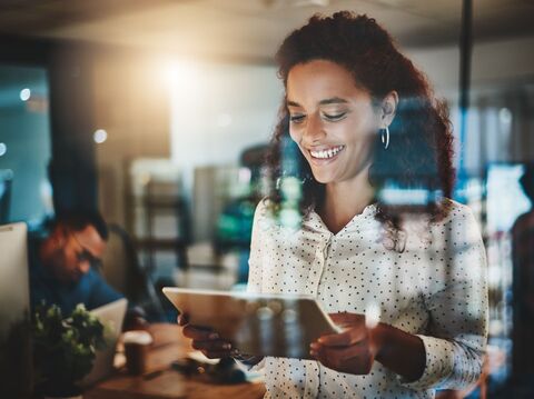 A smiling woman using a tablet in a casual office environment