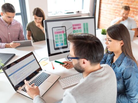 A group of young professionals collaborating around laptops and discussing website designs