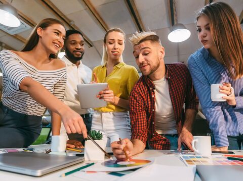 A group of five people were standing near a desk and having a discussion on some graph charts that were kept on the desk