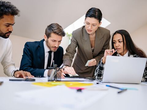 A diverse group of professionals engaged in a discussion around a table with documents and laptops