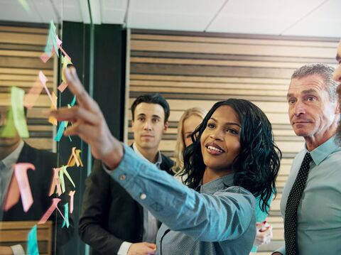 A businesswoman leading a strategy session with colleagues using sticky notes on a glass wall