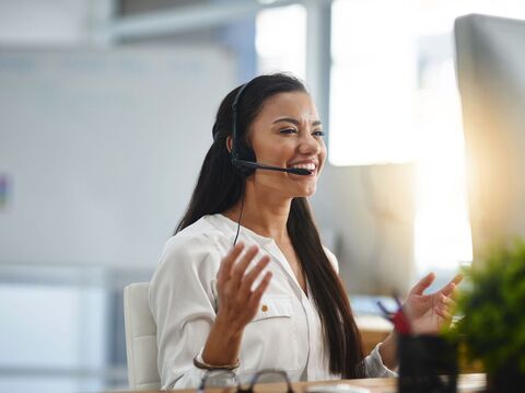 A joyful female customer service representative with a headset speaking and gesturing in a bright office