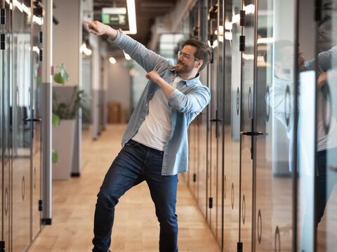  A man dancing joyfully in a modern office hallway, expressing a sense of freedom and creativity