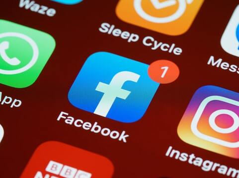 Close-up of a smartphone screen displaying the Facebook app icon among other app icons on a red background