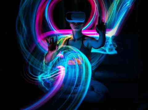 A woman wearing a virtual reality headset surrounded by vivid swirling light trails in a dark room