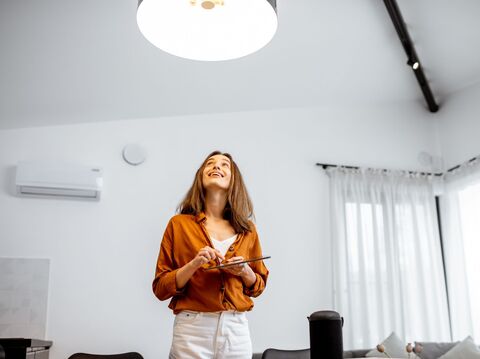 Woman in an orange blouse holding a tablet and looking upwards in a bright, modern living room