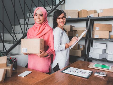 two women in a warehouse setting packing products standing facing opposite directions