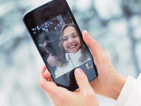 A person's hand holding a smartphone, displaying a video call with a smiling young woman in winter clothing