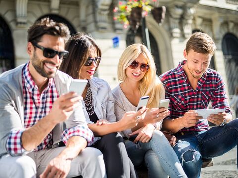 A group of four people sitting on a raised platform and watching their smartphones