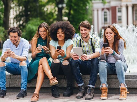 A group of five people are sitting on a raised platform and watching their smartphones