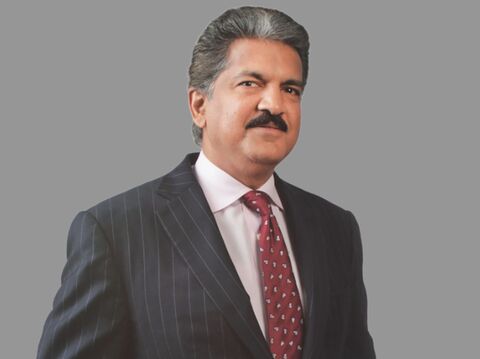 A well-dressed man in a pinstriped suit with a red tie stands confidently against a plain grey background. He has a mustache and a slight smile, exuding a professional demeanor