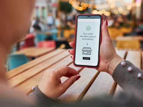 Close-up of a woman's hands holding a smartphone displaying a successful online order confirmation at a cafe