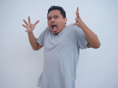 Adult male showing intense emotion of anger or frustration, hands spread wide, in a plain background