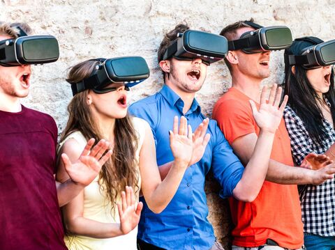 Five people standing against a wall, all wearing virtual reality glasses and reacting with shock